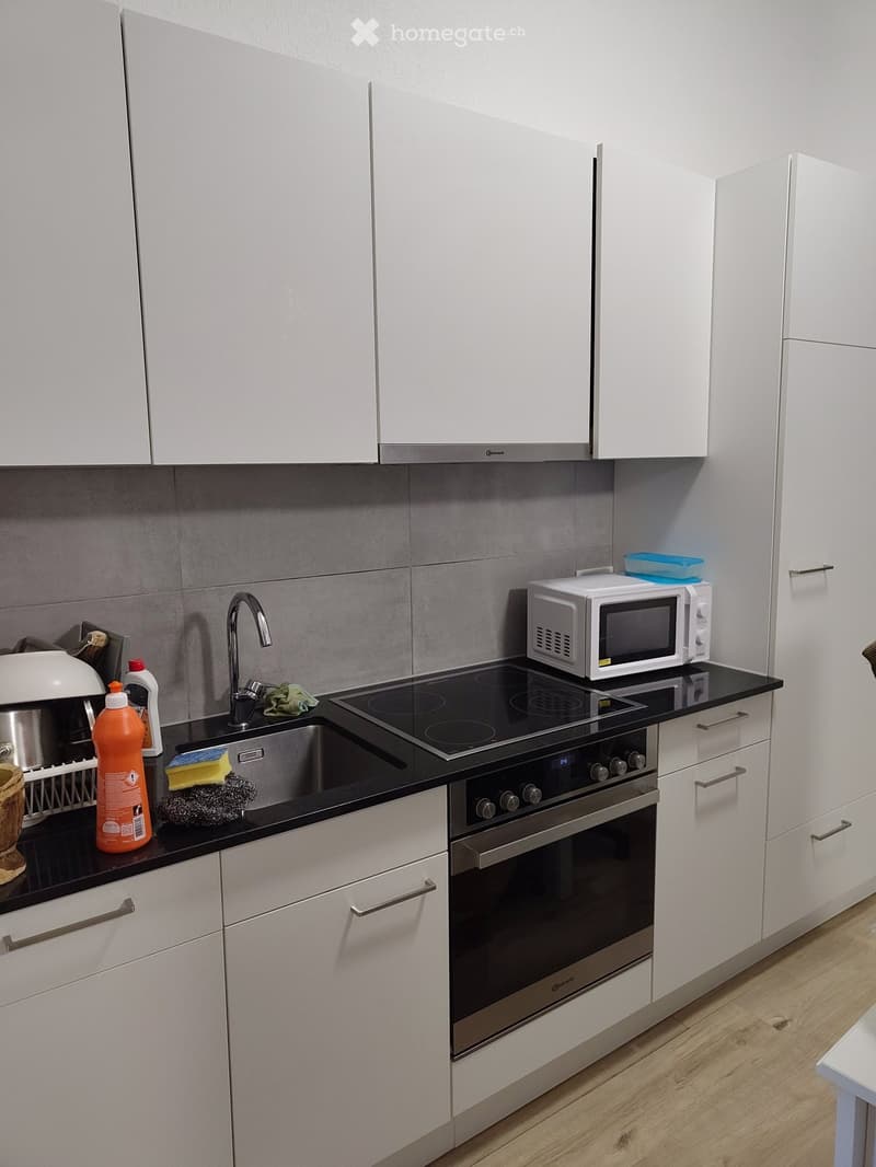 Modern kitchen with white cabinets, stainless steel appliances, and a black countertop.