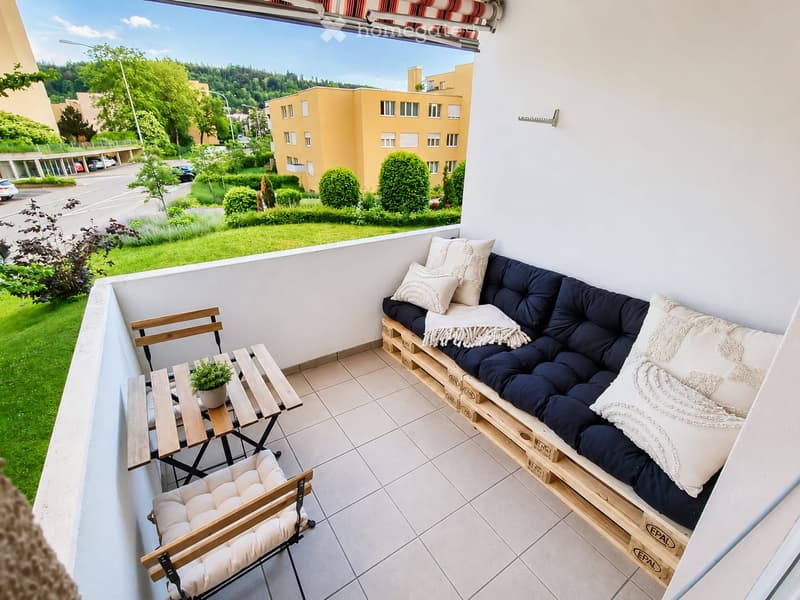 Balcony with a wooden sofa, two wooden chairs, a small table with a potted plant, and a striped awning.