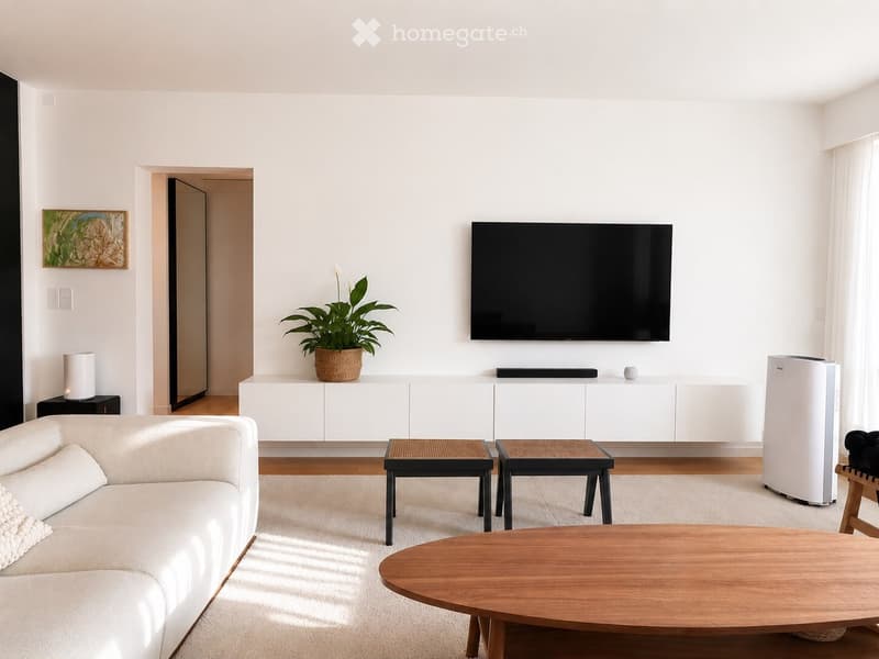 Modern living room with white walls, wooden flooring, a white sofa, a wooden coffee table, two small stools, a potted plant, a mounted TV, and a white cabinet.