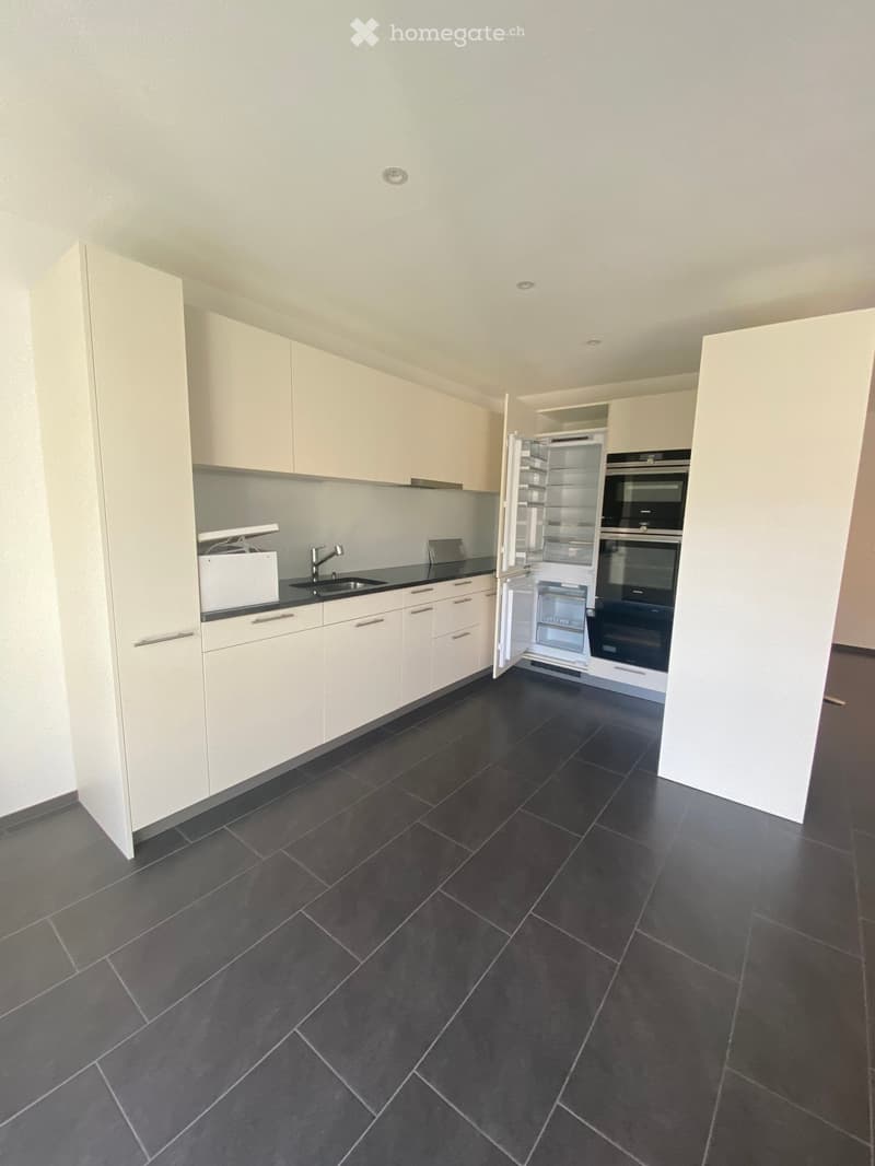 Modern kitchen with white cabinets, dark tiled floor, stainless steel appliances including a refrigerator, oven, and sink.