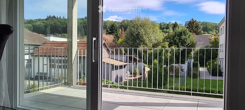 Balcony with metal railing, tiled floor, overlooking a green residential area with houses and trees.