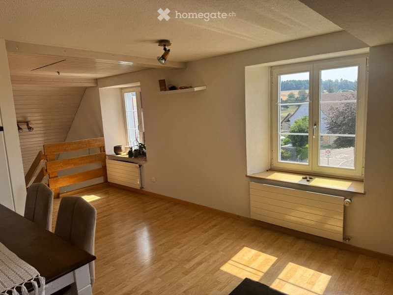 Bright room with wooden flooring, large windows, radiator, bench, table, and chairs.
