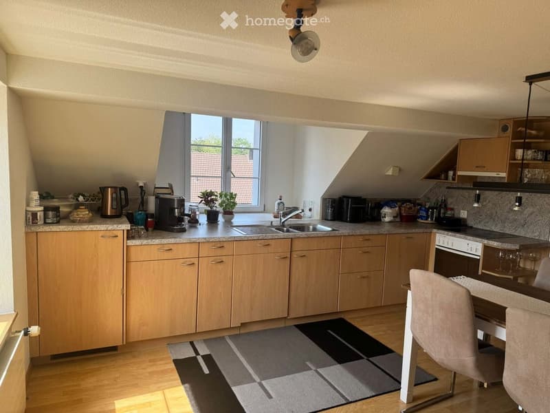 Modern kitchen with light wooden cabinets, granite countertops, stainless steel appliances, and a dining area with a chair and table.