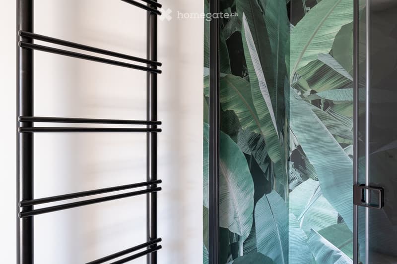 Modern hallway with a glass door featuring a large banana leaf print design and a black metal towel rack with multiple bars.
