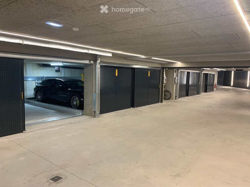 Underground parking area with concrete floors and walls, featuring multiple parking spaces, a single car parked, and a lift entrance.