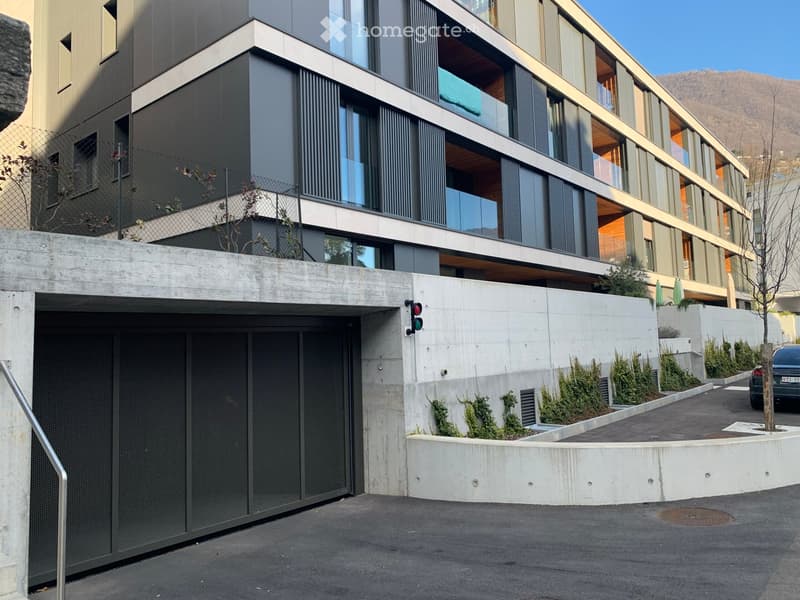 Modern multi-story building with large windows, balconies, and a covered garage entrance.