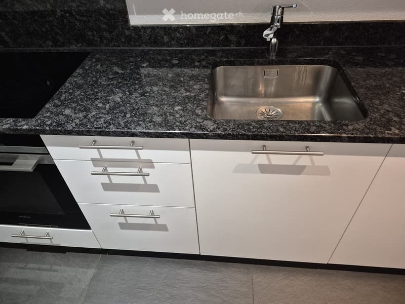 Modern kitchen with white cabinets, stainless steel sink, and granite countertop.