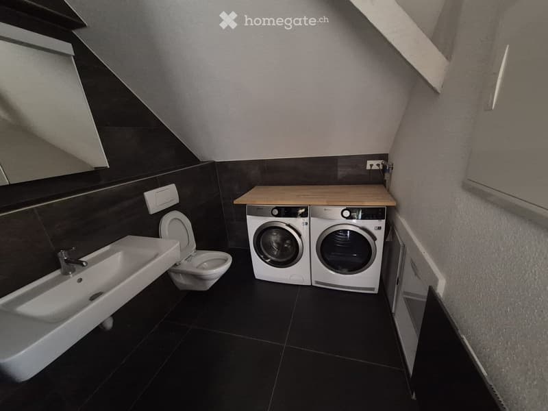 Modern bathroom with a sink, toilet, washing machine, dryer, and a wooden countertop.