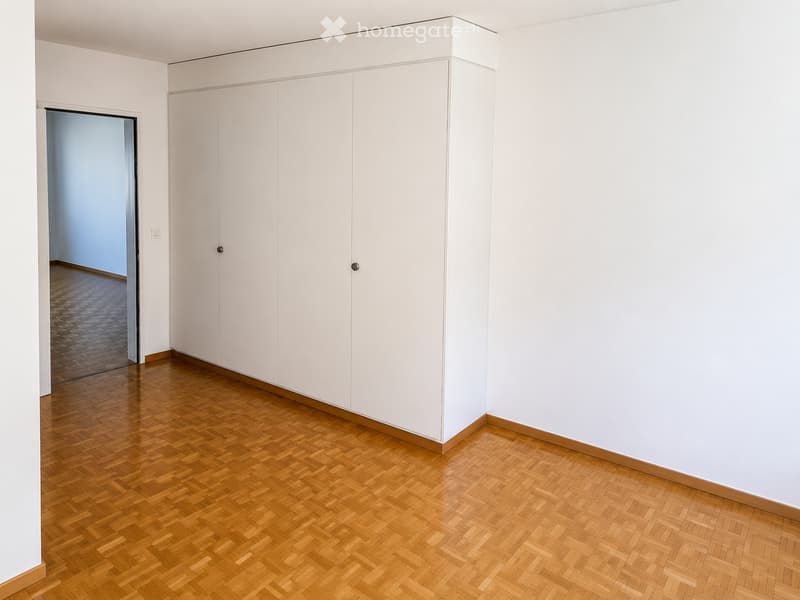 Empty room with white walls, wooden herringbone flooring, and built-in white closet units.
