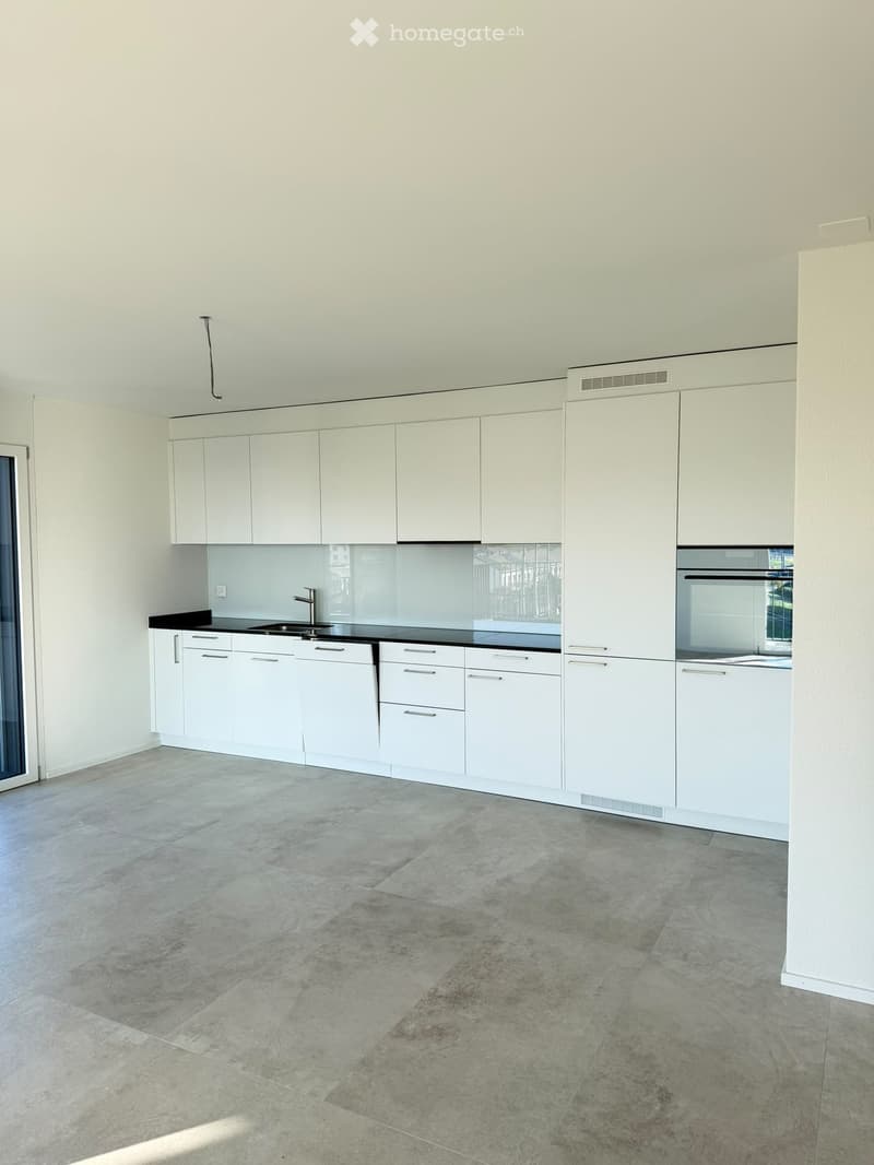 Empty kitchen with white cabinets, black countertops, and a sink, featuring a tiled floor and a large window.