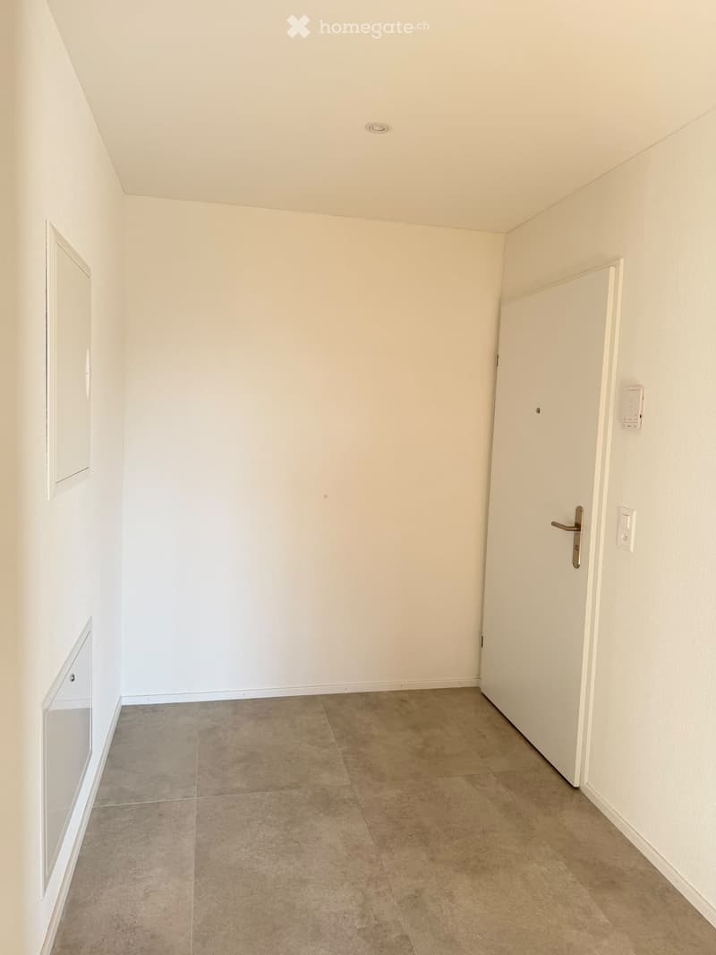 Empty hallway with beige tiled floor, white walls, and a closed door at the end.