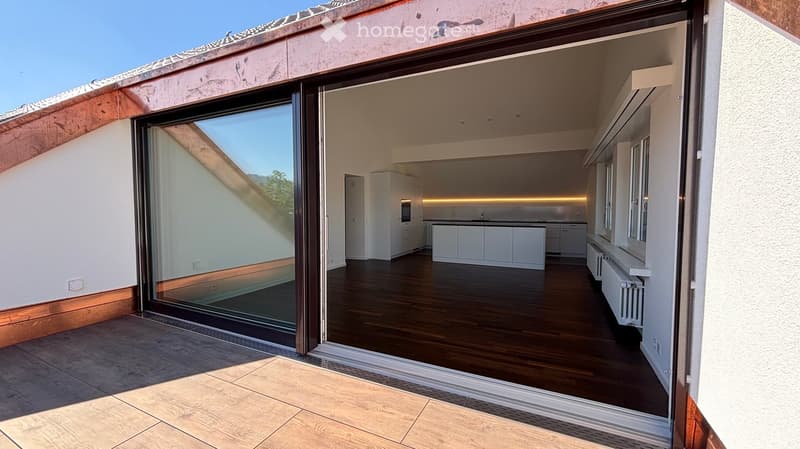 Modern kitchen with white cabinets, a central island, and a sink, connected to a tiled outdoor area through large glass doors.