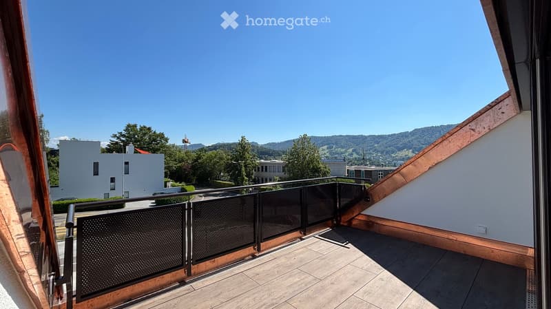 Balcony with wooden decking, metal railing, and scenic view of buildings and mountains.