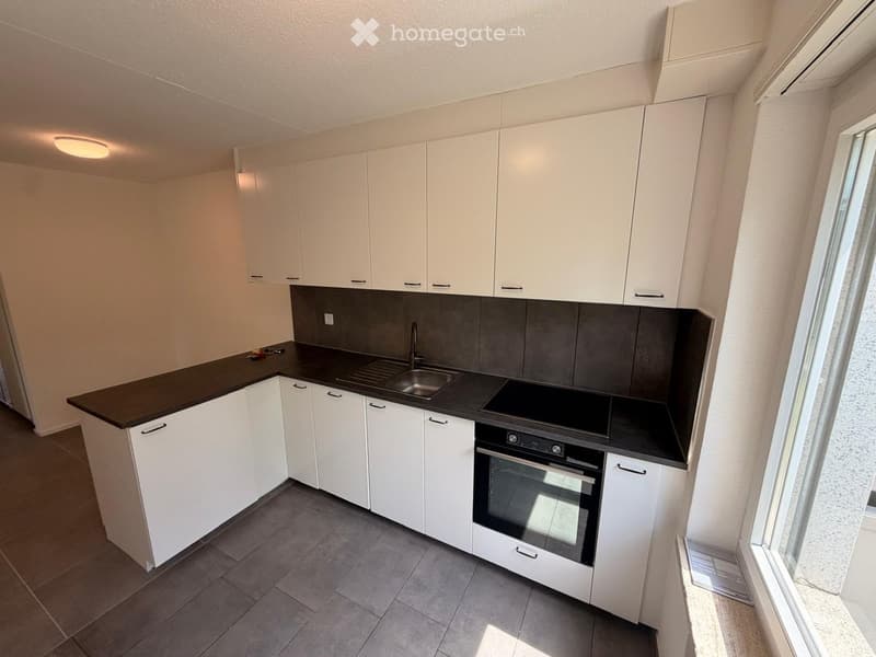 Modern kitchen with white cabinets, dark countertops, and built-in appliances including a sink and oven.