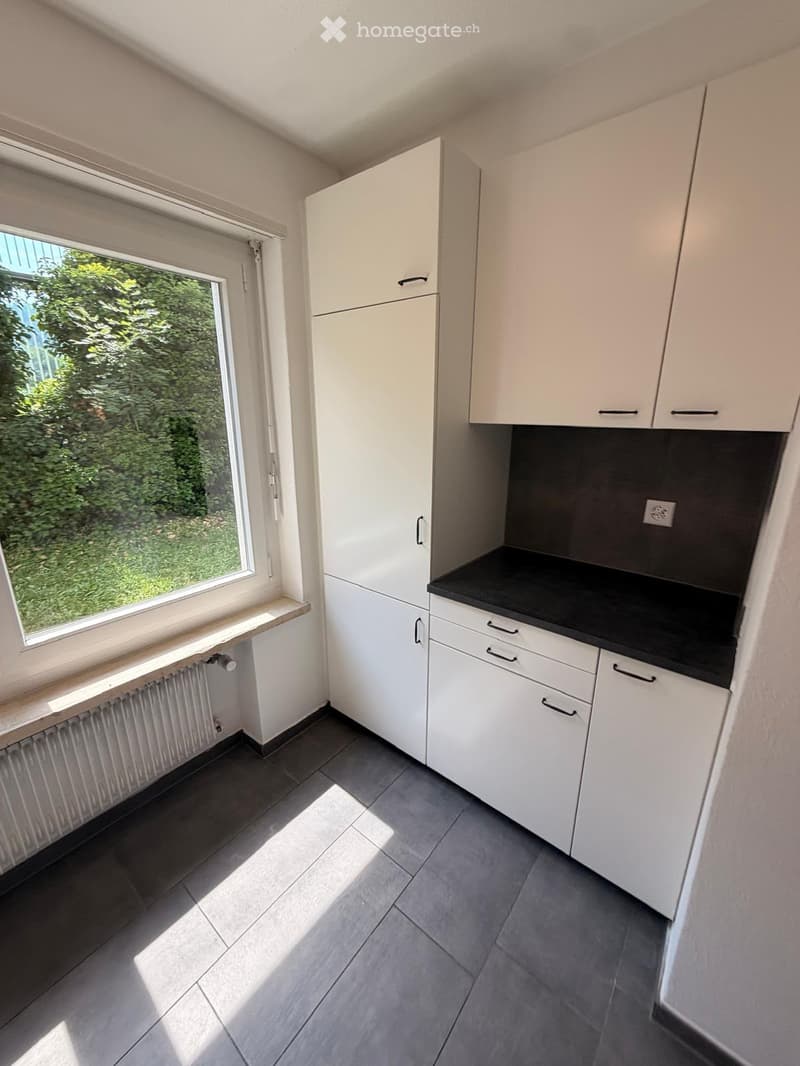 Modern kitchen with white cabinets, black countertop, and a window with a view of greenery.