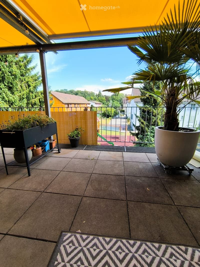 Balcony with tiled floor, rug, potted plants, and garden cart. Features a metal railing and a view of the neighborhood.