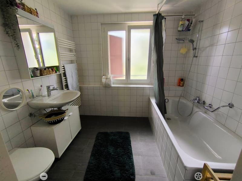 Bathroom with a sink, mirror, bathtub, toilet, and a window. Includes a towel rack, shower, and various toiletries.