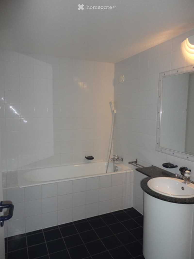 Modern bathroom with white tiled walls, black tiled floor, bathtub, sink, and mirror.