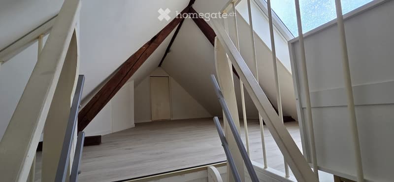 Empty attic space with wooden floor, exposed wooden beams, and skylight windows.
