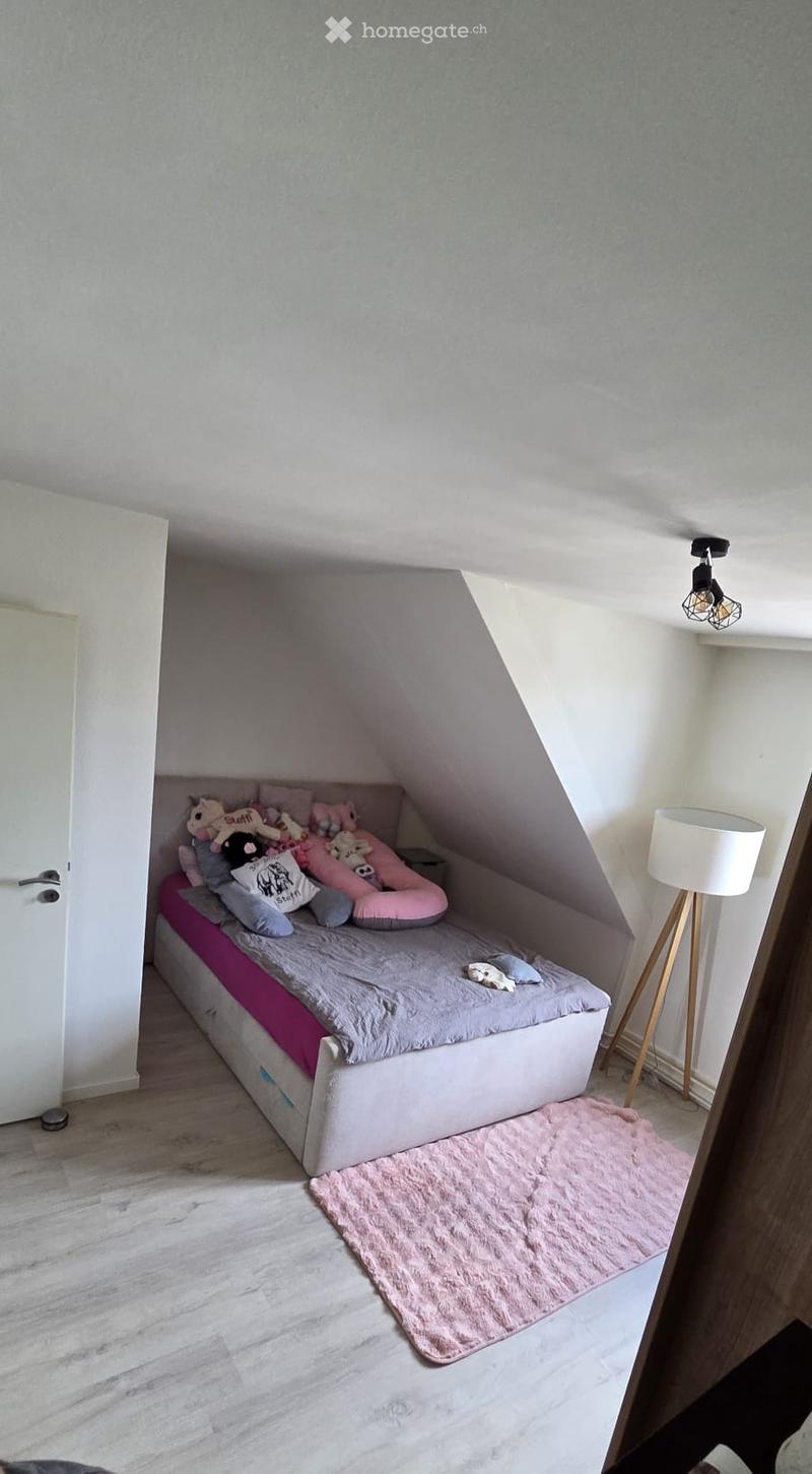 Cozy attic bedroom with a single bed, pillows, a blanket, toys, a pink rug, and a floor lamp.