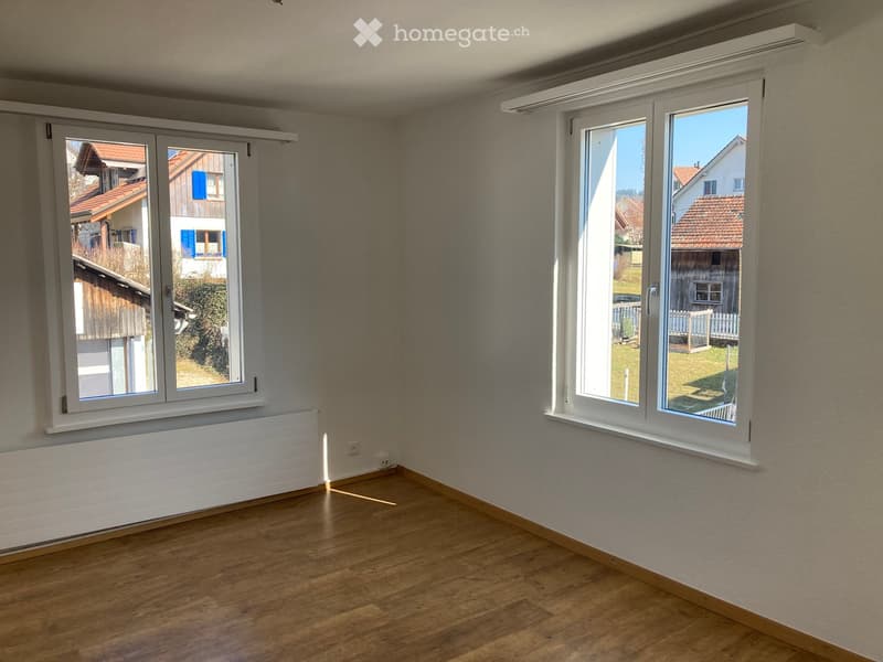 Empty room with wooden flooring, large windows, and radiators beneath the windows.