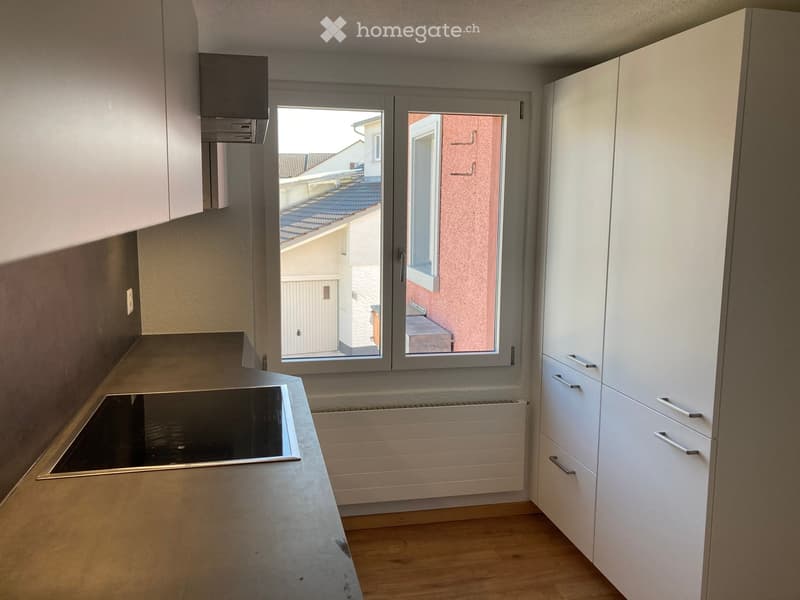 Modern kitchen with white cabinets, a countertop, and an induction stove, featuring large windows with a view of the building exterior.
