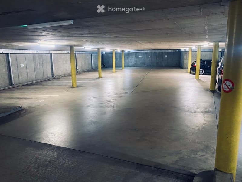 Underground parking area with concrete floors and walls, yellow support pillars, and a few parked cars visible in the background.