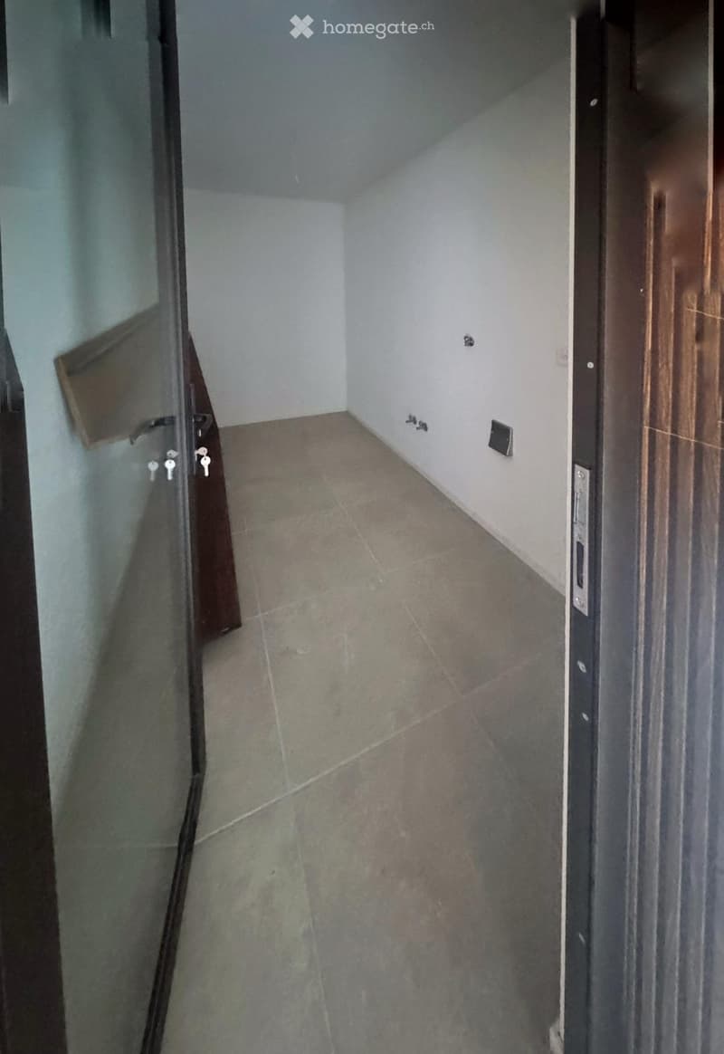 Empty hallway with tiled floor and white walls, featuring a glass door and a wooden door frame.