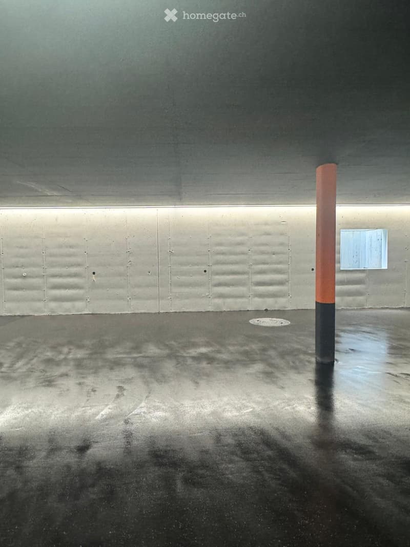 Empty room with a concrete floor and walls, a single orange and black pole, and a small square sign on the wall.