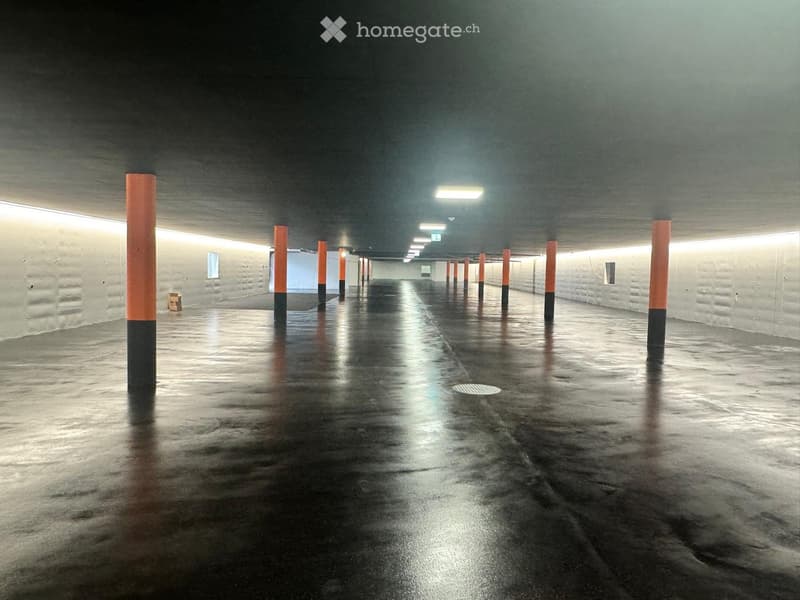 Empty underground corridor with concrete walls, orange and black support columns, and a smooth, reflective floor.