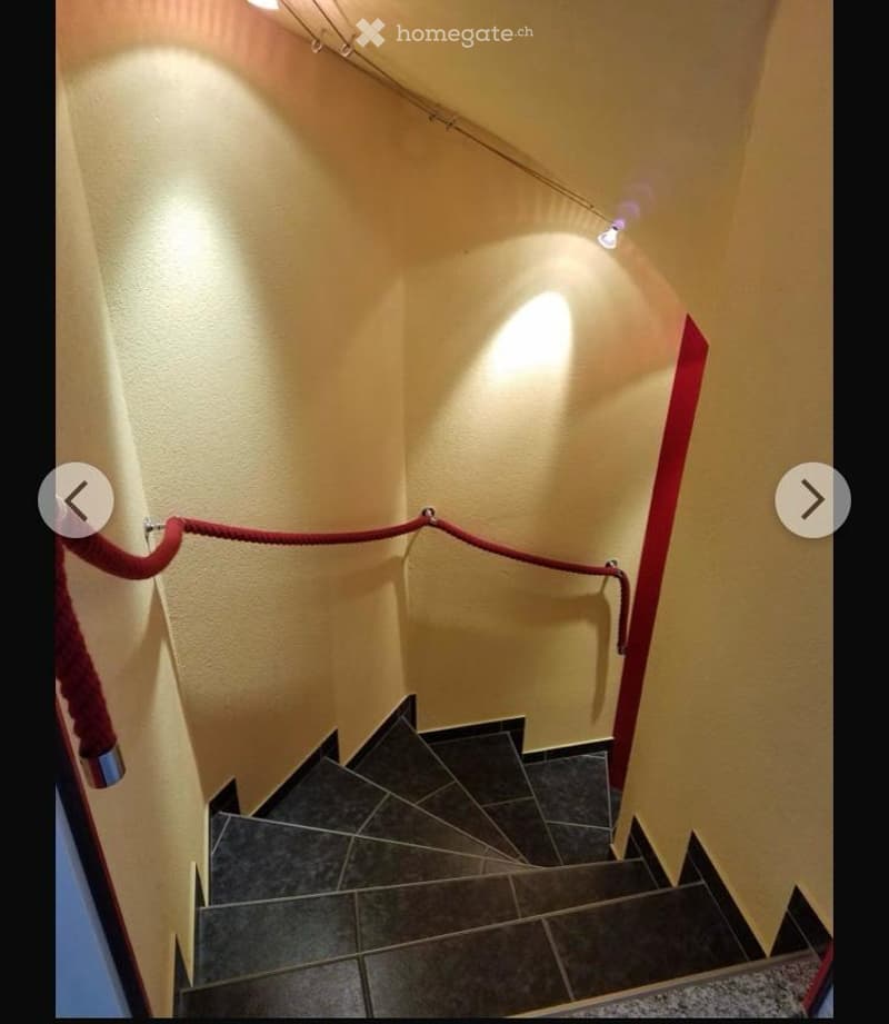 Spiral staircase with dark tiled steps, red rope handrail, and wall-mounted lighting fixtures.