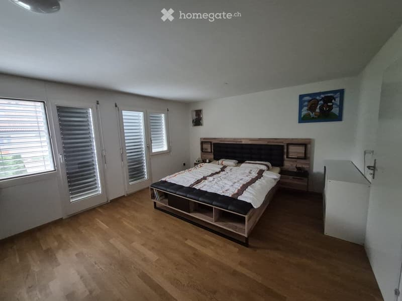 Modern bedroom with wooden flooring, large bed with headboard, nightstand, and artwork on the walls.