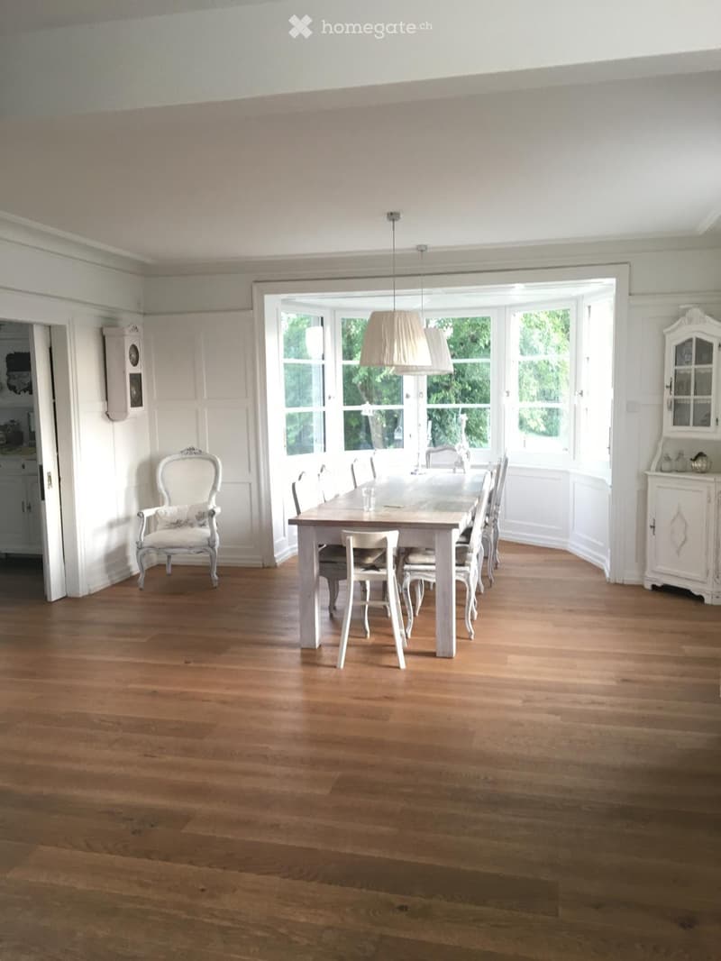 Dining room with wooden floor, white walls, large windows, and a table and chairs.