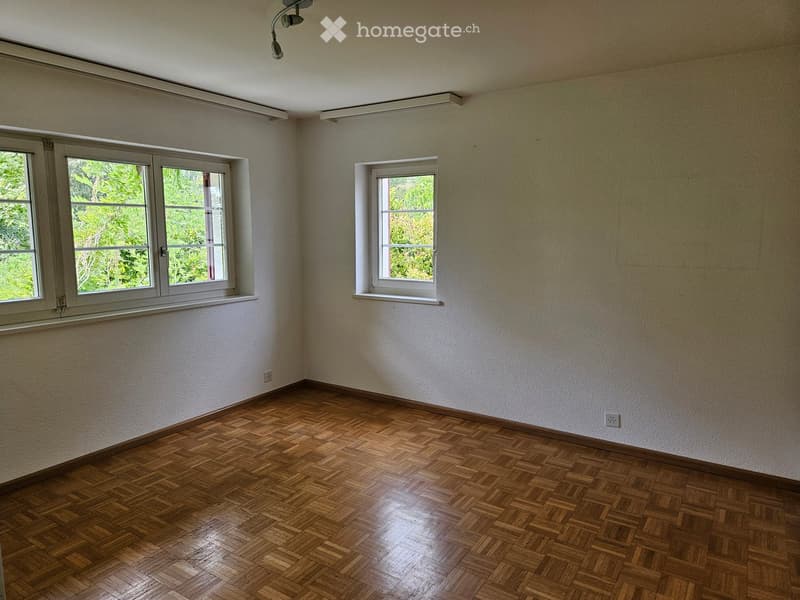 Empty room with wooden parquet flooring, white walls, and multiple windows allowing natural light.