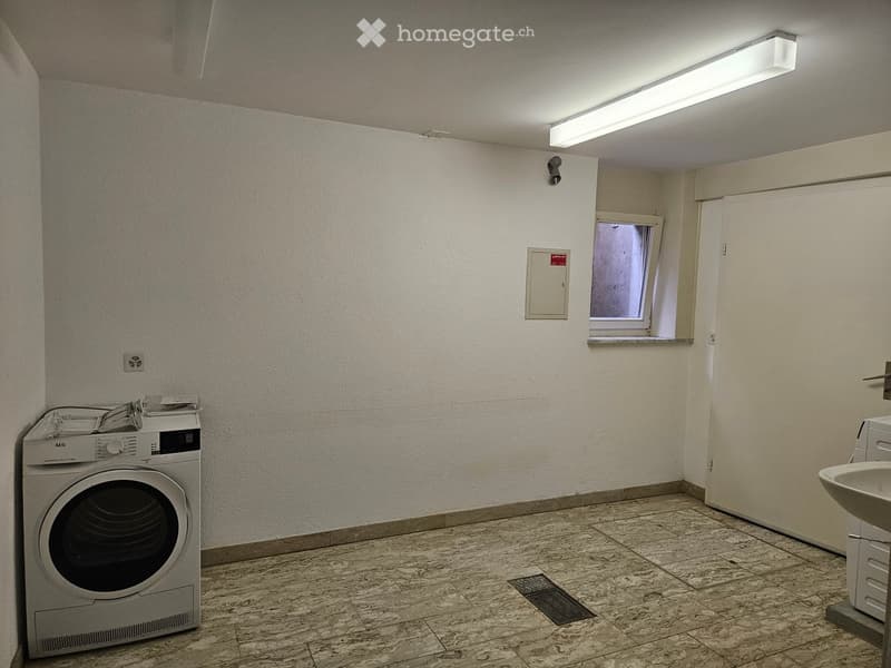 Bathroom with a washing machine, sink, tiled floor, and a small window.