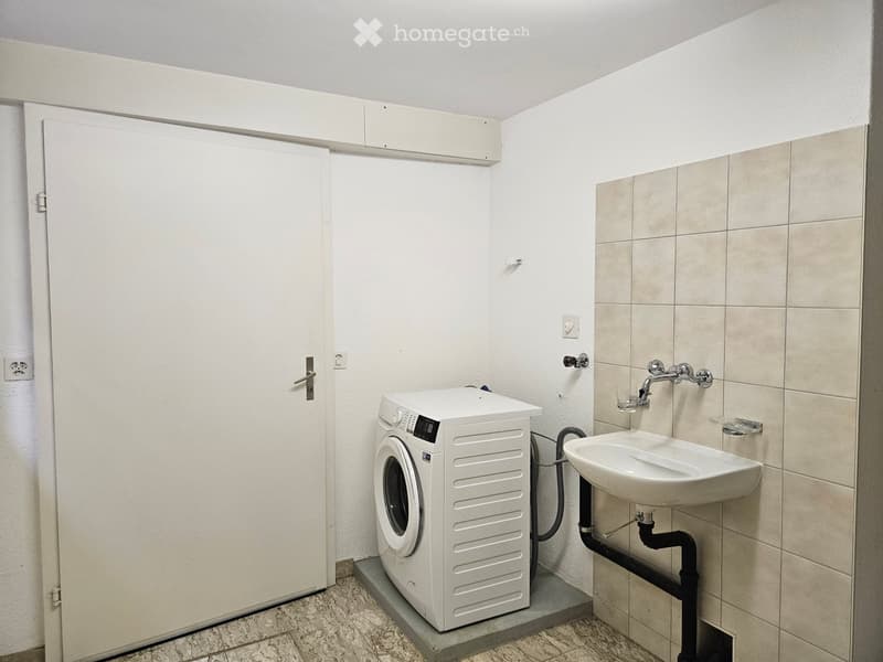 Bathroom with a white washing machine, a sink, tiled walls, and a door.
