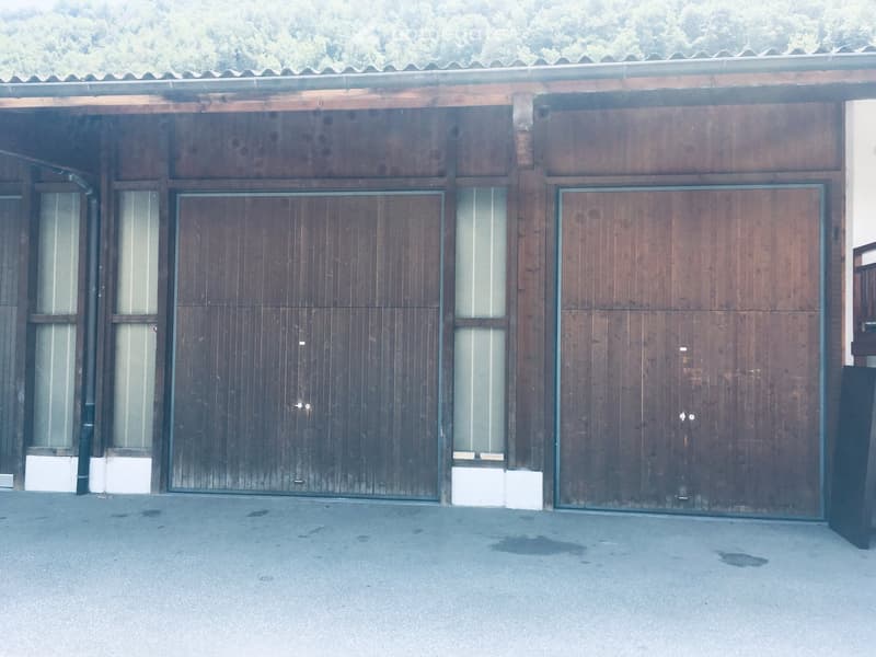 Wooden building with large garage doors and small windows, situated on a paved surface.