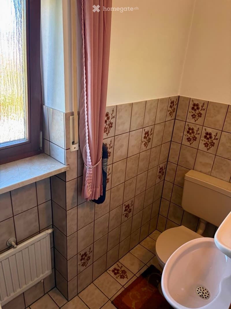 Bathroom with tiled walls and floor, a toilet, a sink, and a pink curtain on the window.