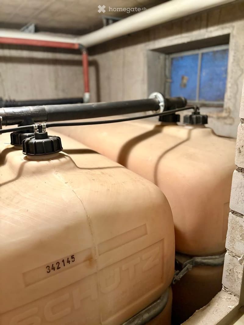 Underground water storage area with multiple large beige water tanks, visible pipes, and a small window with blue glass.