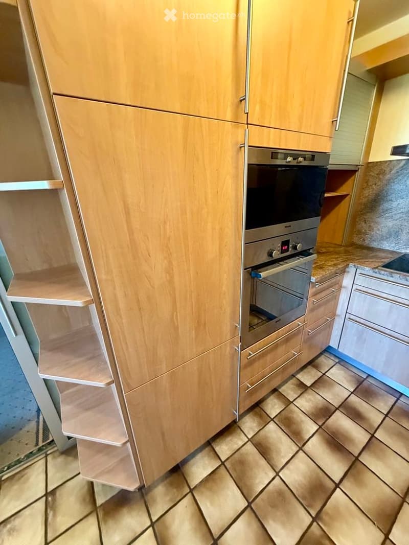 Modern kitchen with light wooden cabinets, stainless steel oven, tiled floor, and countertop.