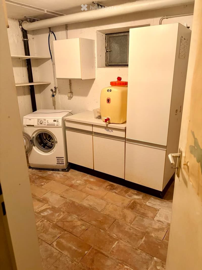 Utility room with a washing machine, cabinets, and a water tank on a tiled floor.