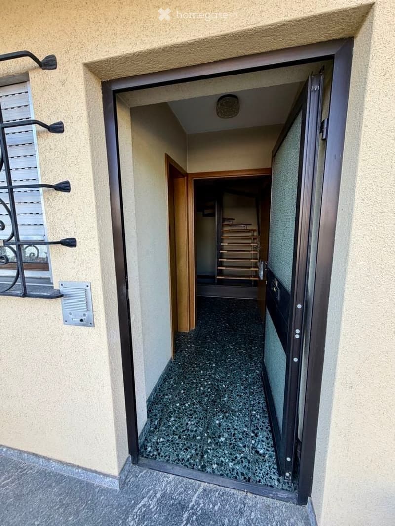 Entrance to a hallway with a tiled floor, wooden doors, and a visible staircase in the background.