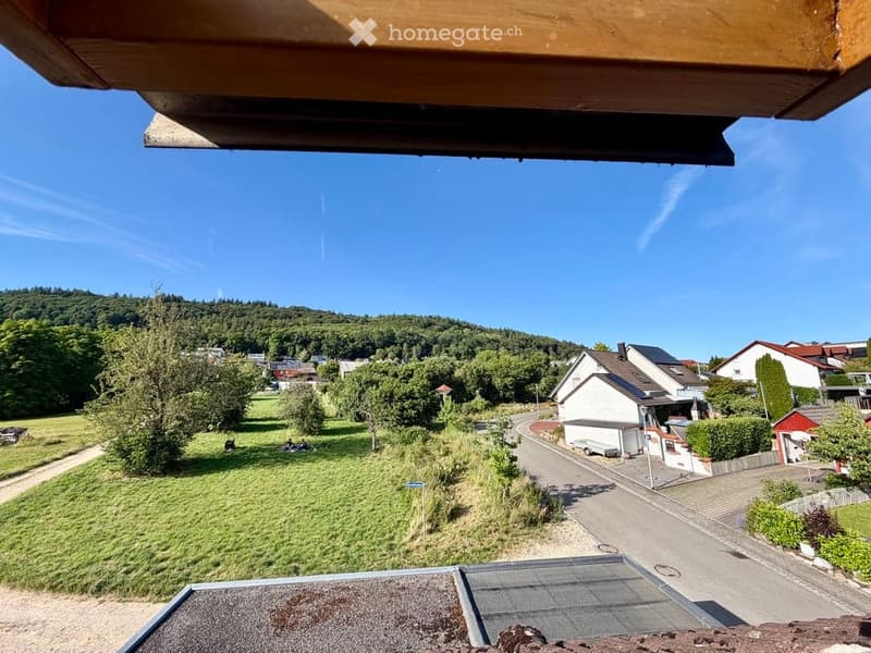 Balcony view overlooking a suburban neighborhood with houses, trees, and a grassy field under a clear blue sky.