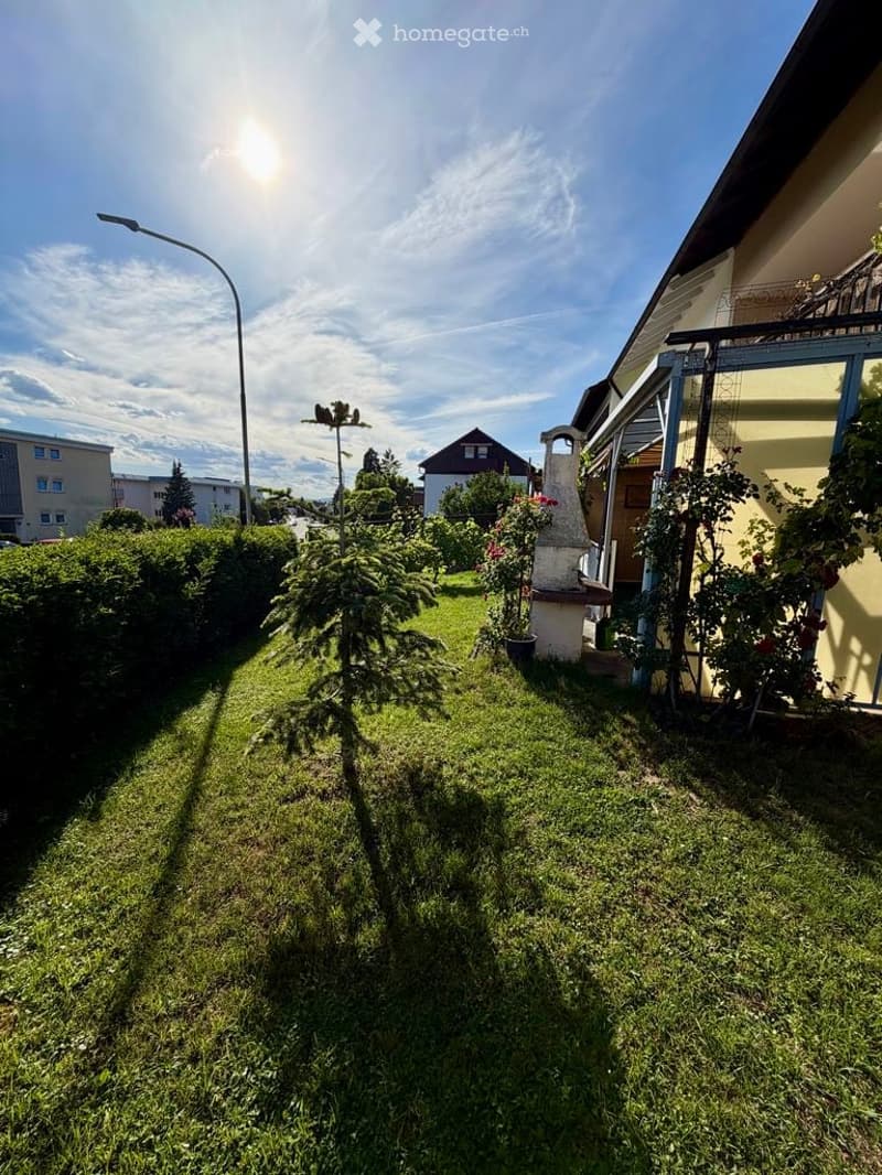 Well-maintained garden with green grass, trimmed hedges, small trees, and a decorative stone structure near the house.