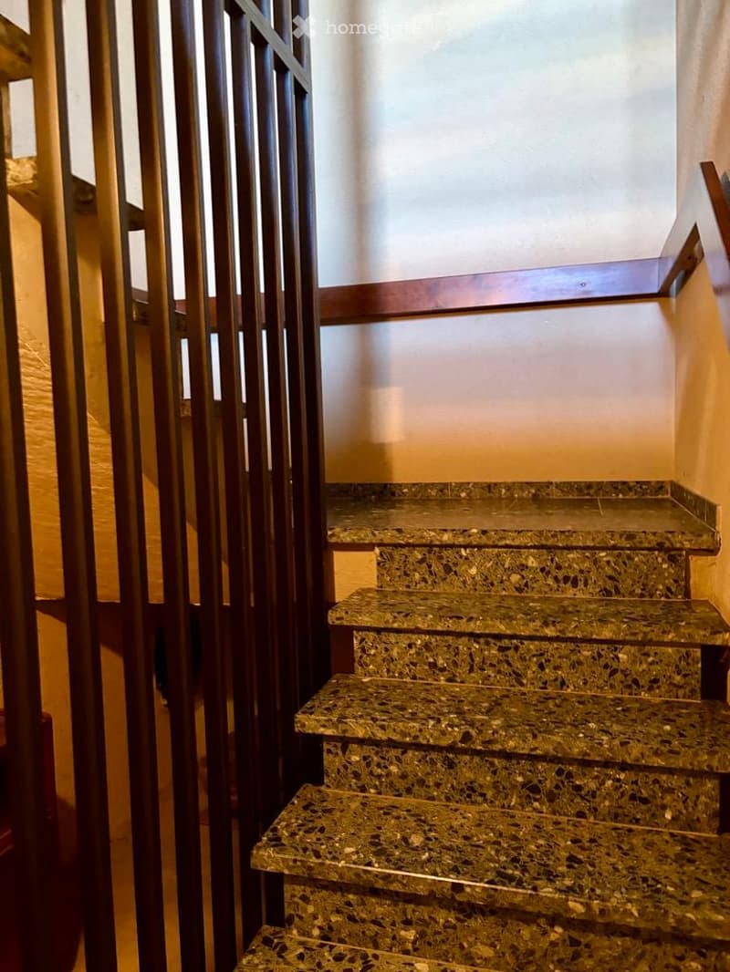 A staircase with polished marble steps and a wooden handrail, featuring a modern metal gate for safety.