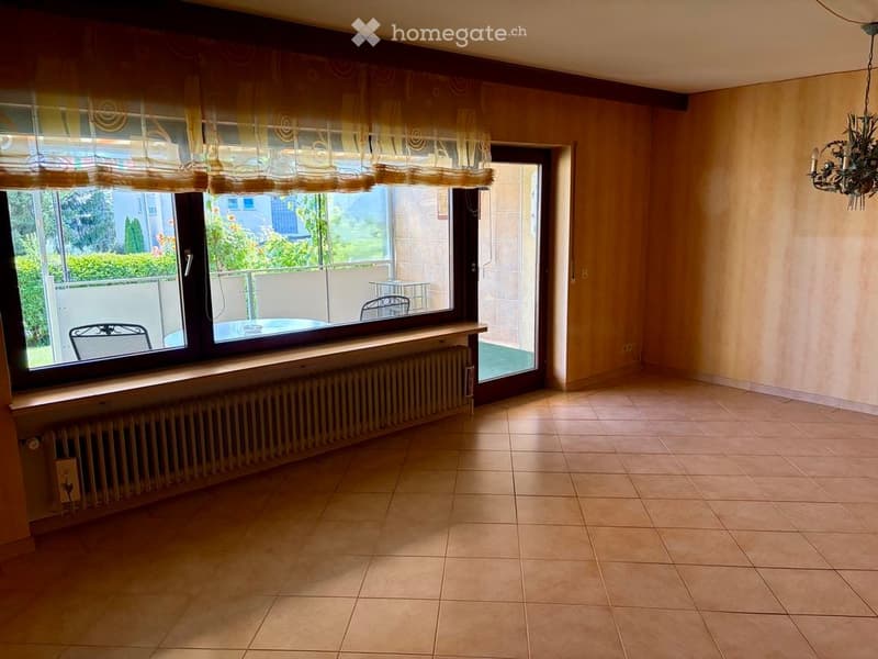 Empty room with tiled floor, large window with balcony access, radiator, and chandelier.