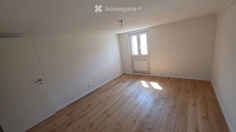 Empty room with wooden flooring, white walls, and a single window with a radiator below it. No furniture or personal items are present.