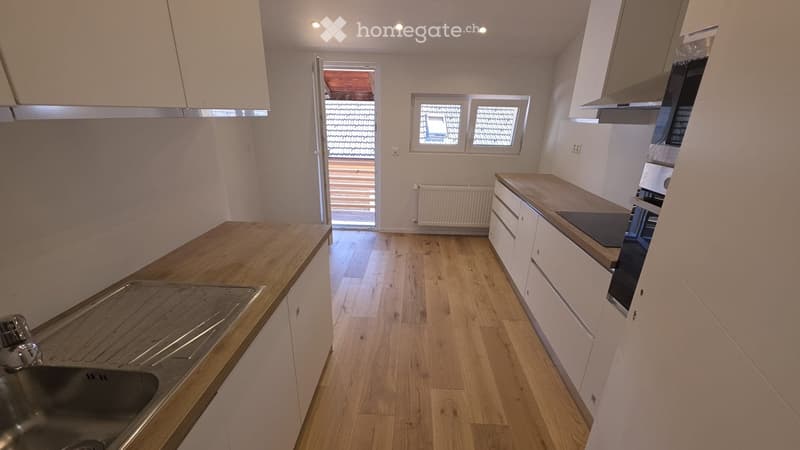 Modern kitchen with light wooden flooring, white cabinets, and a wooden countertop. Features a sink, built-in appliances, and a radiator near the window.