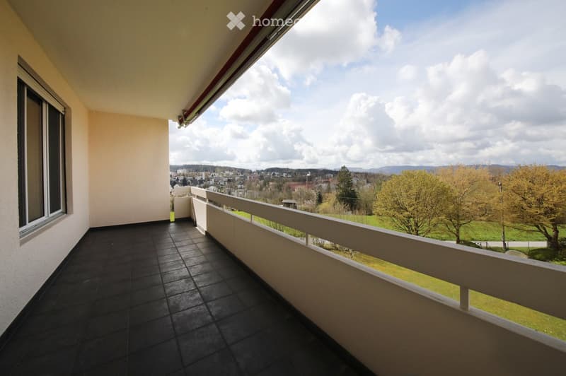 Balcony with dark tiled floor, white railing, and scenic view of a town and green landscape.