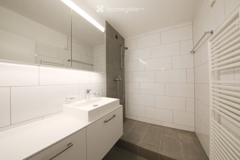 Modern bathroom with white tiles, a large mirror, a sink with a modern faucet, a shower area, and a white radiator.